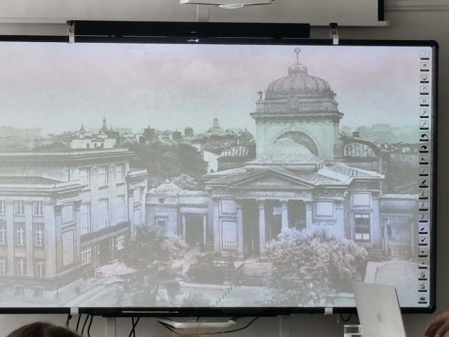 uczniowie siedzący na krzesłach słuchają wypowiedzi mężczyzny