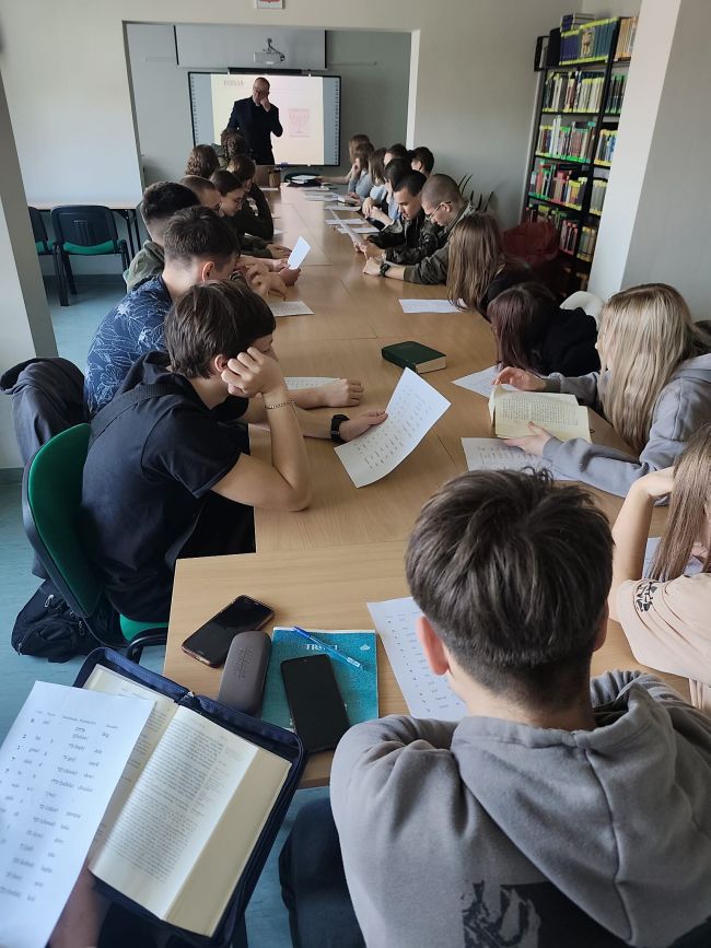 młodzi ludzie przy długim stole, czytający kartki