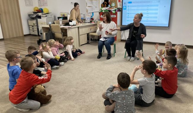 Dzieci siedzą na podłodze , rozmawiają z prowadzącymi zajęcia