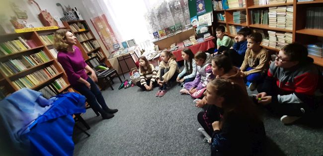 Biblioteka szkolna. Uczniowie siedzą na dywanie w półokręgu. Prowadząca prezentuje teatrzyk Kamishibai.
