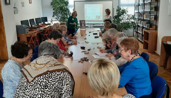 Na zdjęciu słuchacze Uniwersytetu Trzeciego Wieku siedzący przy stolikach wraz z prowadzącymi zajęcia