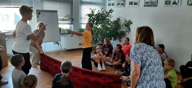 Nauczyciele prowadzą zabawę dla dzieci, uczniowie siedzą na podłodze.
