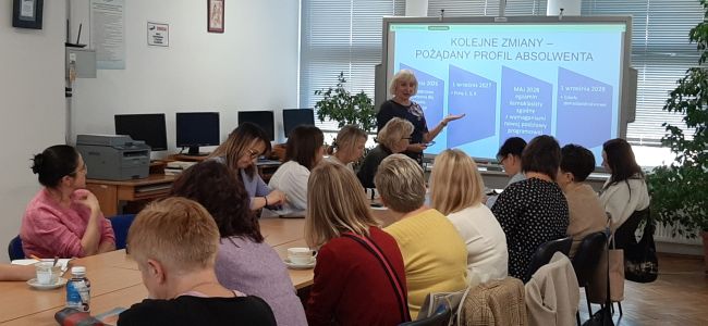 Prowadząca stoi przy tablicy interaktywnej, wyświetla prezentację. Nauczyciele siedzą przy stole,
notuja.