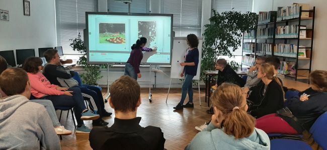 Prowadzaca przy tablicy interaktywnej. Uczniowie siedzą w kręgu, słuchają.
