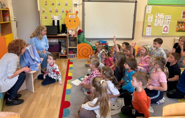 Dzieci siedzą na podłodze, nauczyciele czytają opowiadanie z wykorzystaniem kamishibai.