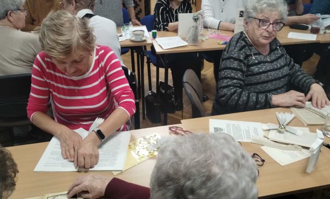 Uczestnicy warsztatów siedzą przy stołach i wykonują prace.