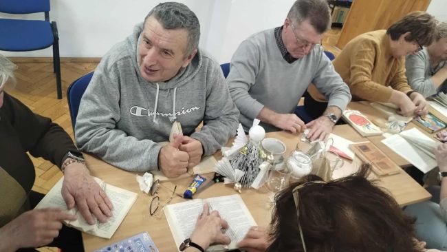 Uczestnicy warsztatów siedzą przy stołach i wykonują prace.