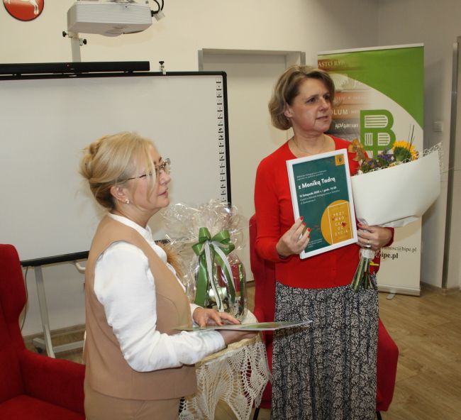 Monika Tadra z pamiątkowym plakatem oraz bukietem wręczonymi przez wicedyrektora biblioteki.