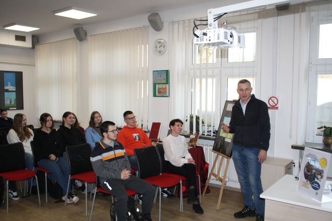 Podróżnik Jacek Podkościelny oraz uczestnicy spotkania zgromadzeni w czytelni biblioteki.
