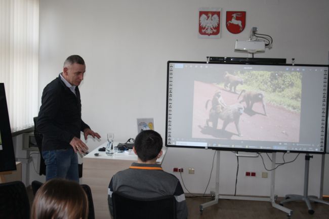 Podróżnik Jacek Podkościelny opowiada o Afryce podczas spotkania w bibliotece, omawia zdjęcia wyświetlane na tablicy multimedialnej.