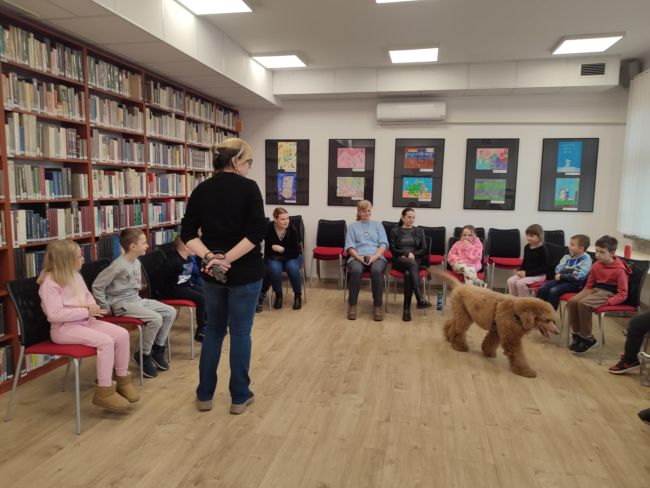 pies chodzi po sali, na krzesełkach siedzą dzieci