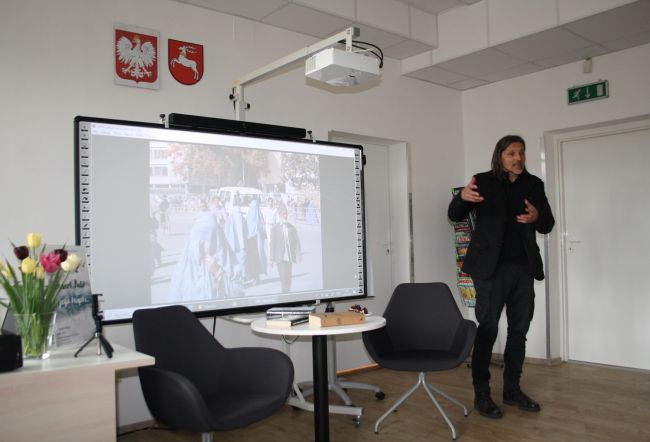 Robert Kulik opowiada o swoim pobycie na misji w Afganistanie, na tablicy multimedialnej jest wyświetlone zdjęcie pokazujące ludzi z tego kraju.
