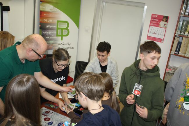 Gracze podchodzą do stolika prowadzących, aby kupić produkty i odbyć handlowe podróże na planszy do gry.