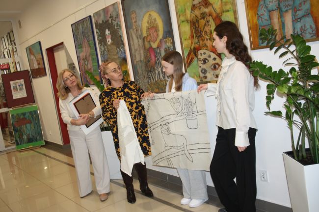 Goście finisażu pokazują przykładowe płótno, na którym stosuje się technikę batiku.