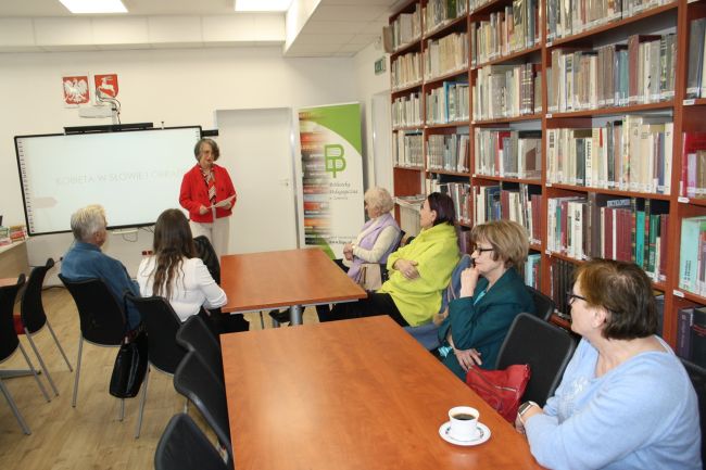 Wybrane książki z księgozbioru biblioteki z motywem kobiety ustawione na biurku, tuż za nimi w wazonie czerwone tulipany.