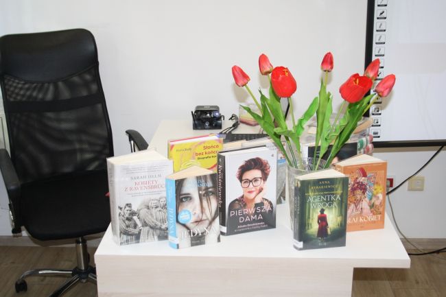 Dyrektor biblioteki dr Dorota Mach wygłasza prelekcję na temat kobiet w literaturze i malarstwie, której przysłuchują się seniorzy zebrani na kolejnym spotkaniu z cyklu